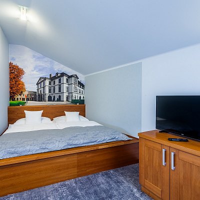 Standardní pokoj hotelu Jelínkova vila - útulná část pokoje s postelí, televizí a plakátem na zdi